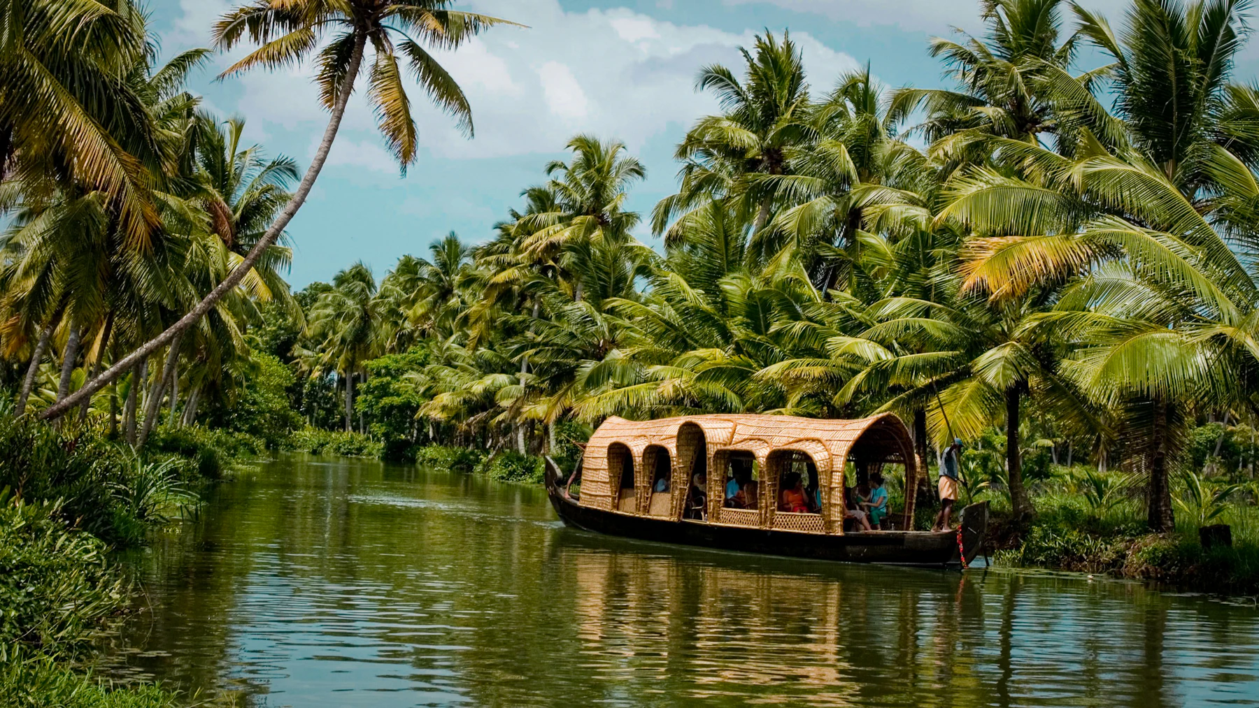 A wooden boat moving through the palm-lined backwaters of Kerala